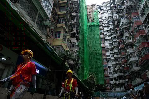 Construction workers walk past a building under renovation in Quarry Bay district after the deadly fire at Wang Fuk Court, in the Tai Po district of Hong Kong's New Territories, Thursday, Dec 4, 2025.